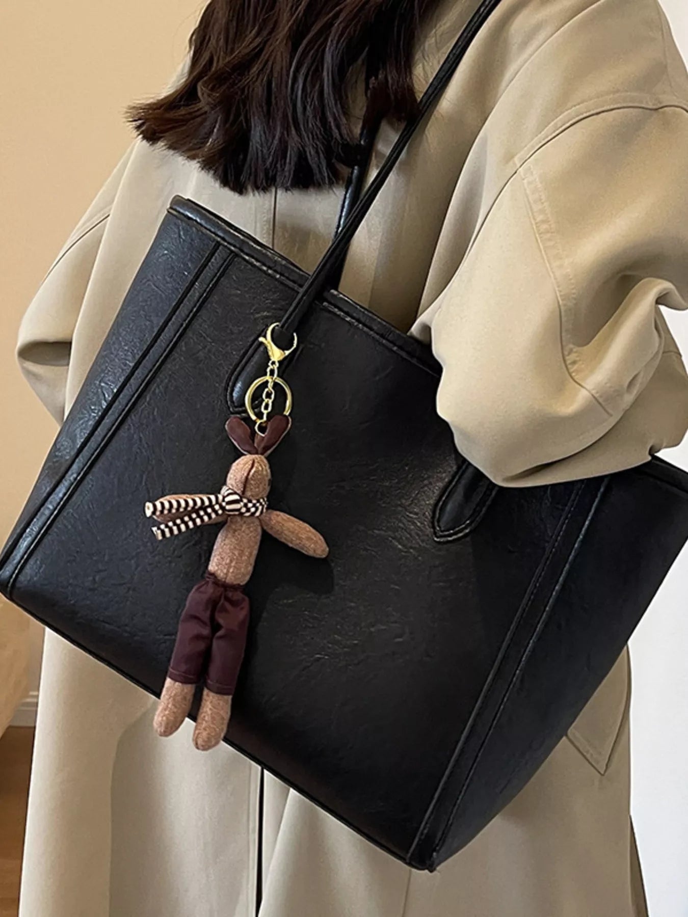 Black leather tote on shoulder, structured shape, front zipper pocket, plush charm and tassel