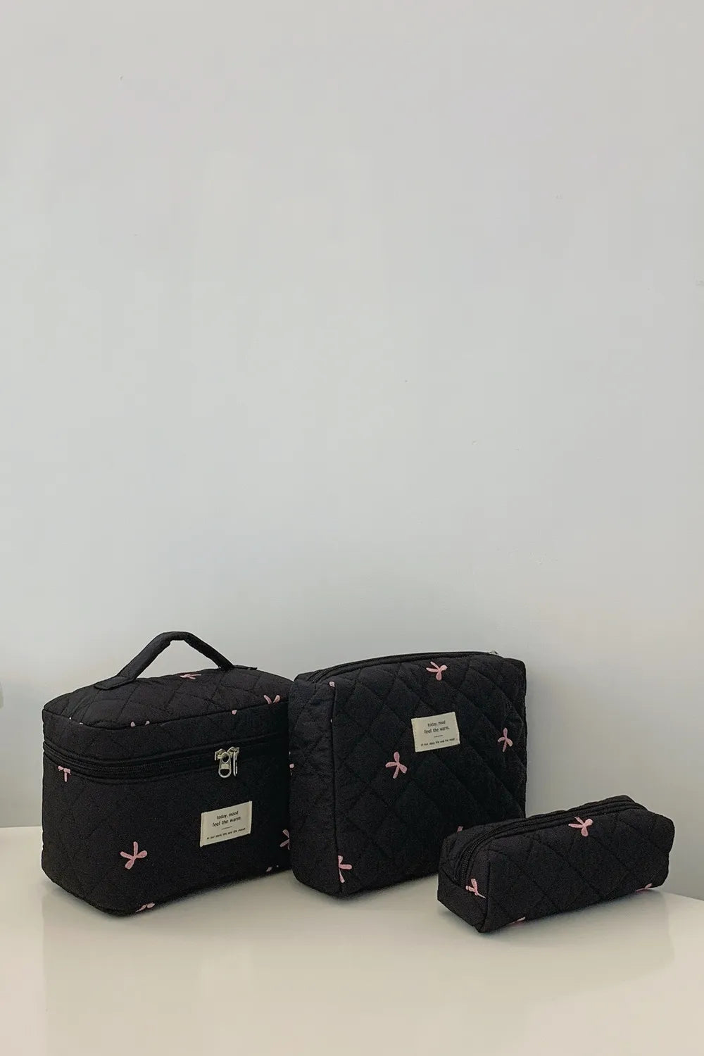 Black quilted storage bags set with bow accents, label patches, and zipper openings.
