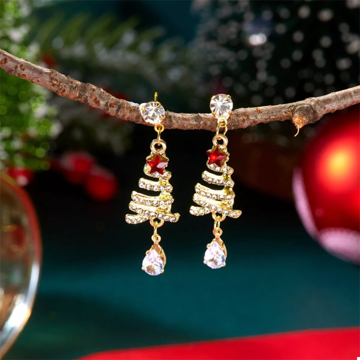 Gold-tone Christmas tree earrings with red star top, glitter rows, and clear teardrop dangles