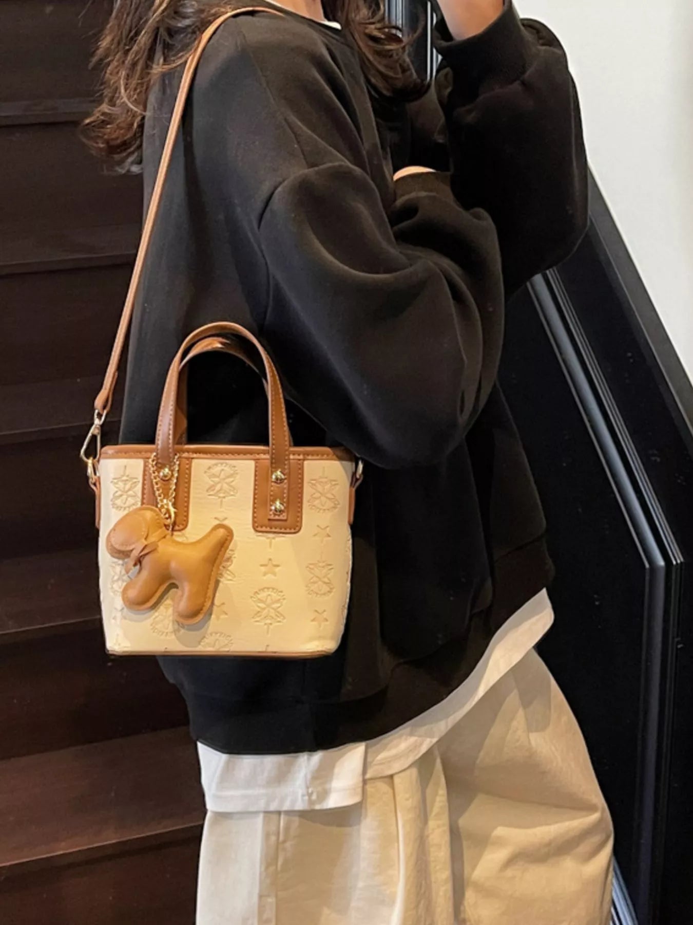 Beige Umhängetasche mit Reliefmuster, braunen Griffen und hängendem Hund-Charm
