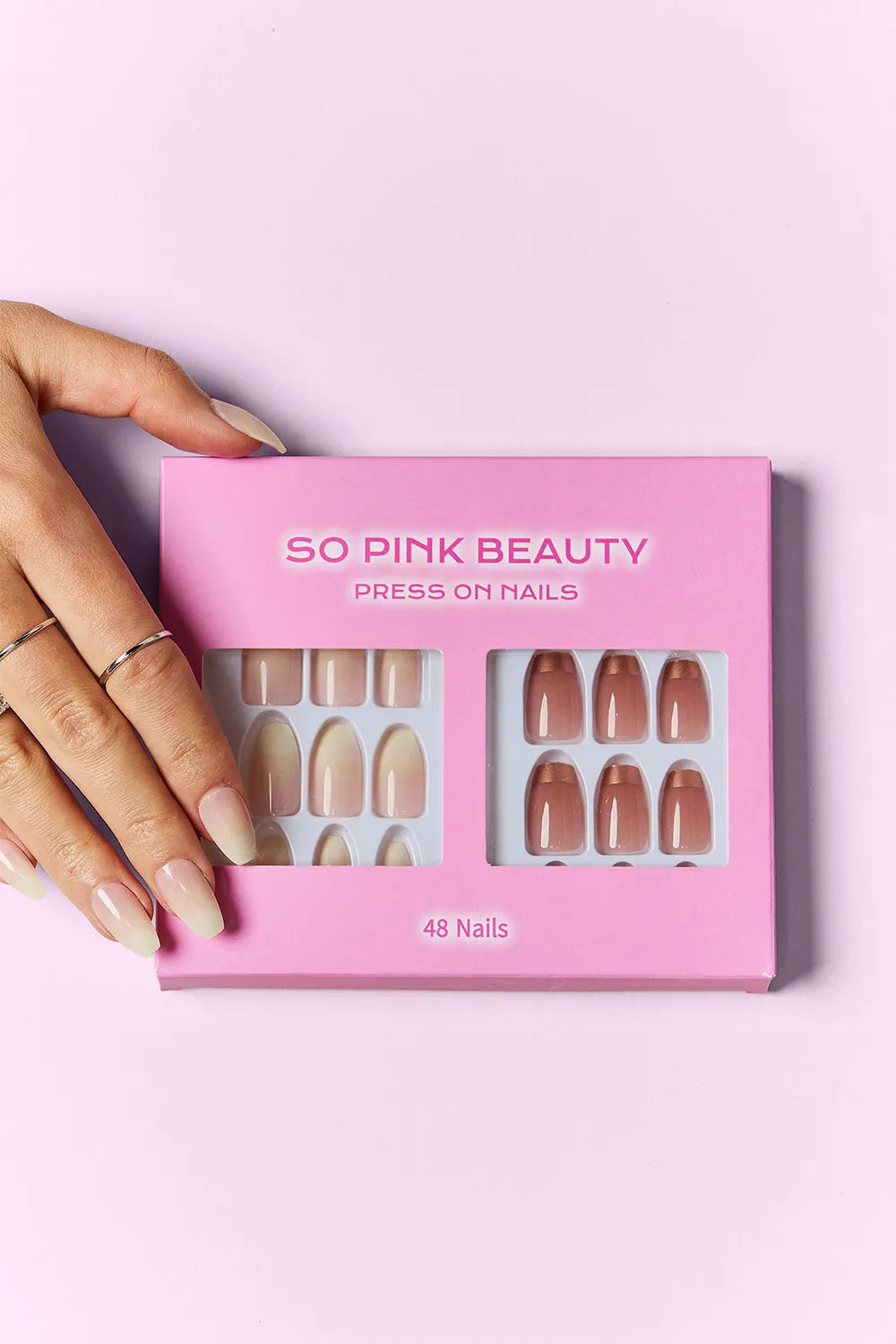 Hand holding SO PINK BEAUTY press-on nails box, 48 nails, mixed nude shade designs