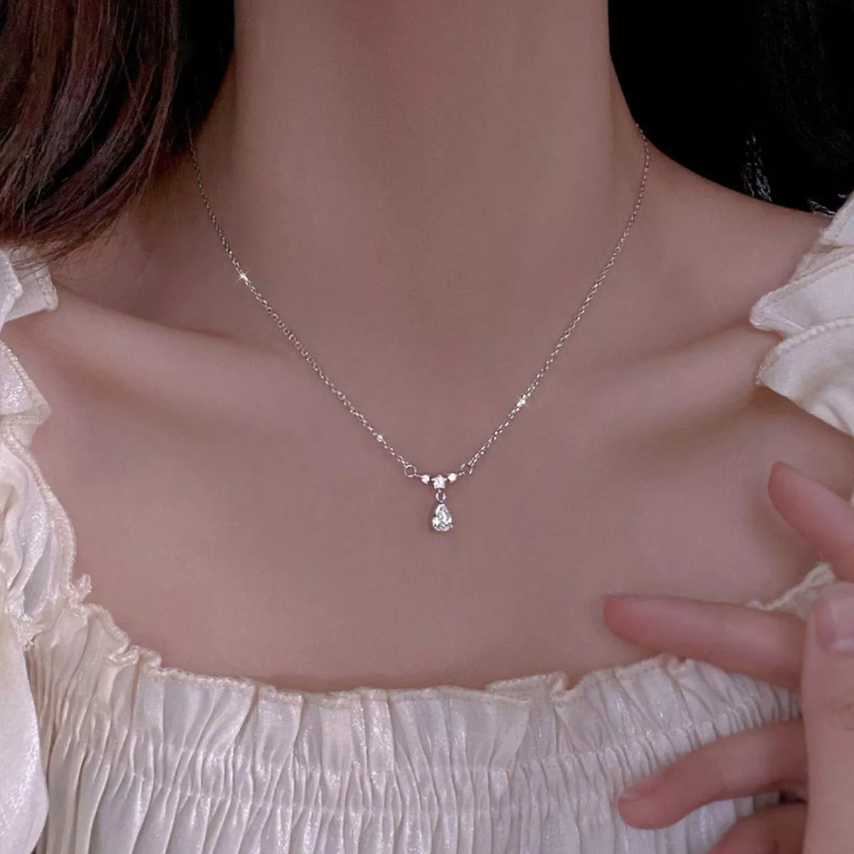 Sterling silver teardrop zircon necklace worn on model, featuring a small stone cluster and drop