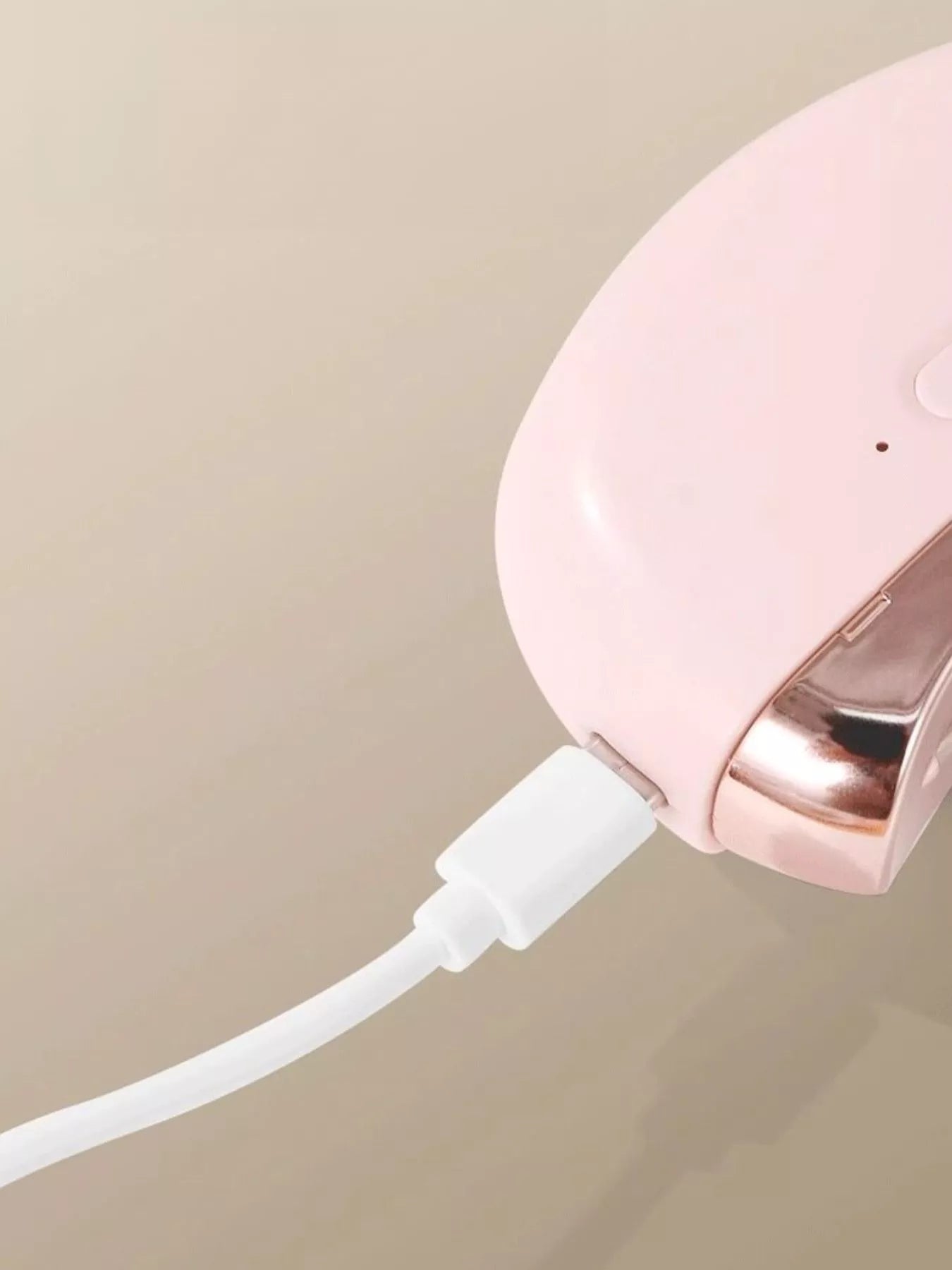 Blush pink electric nail buffer connected to charging cable