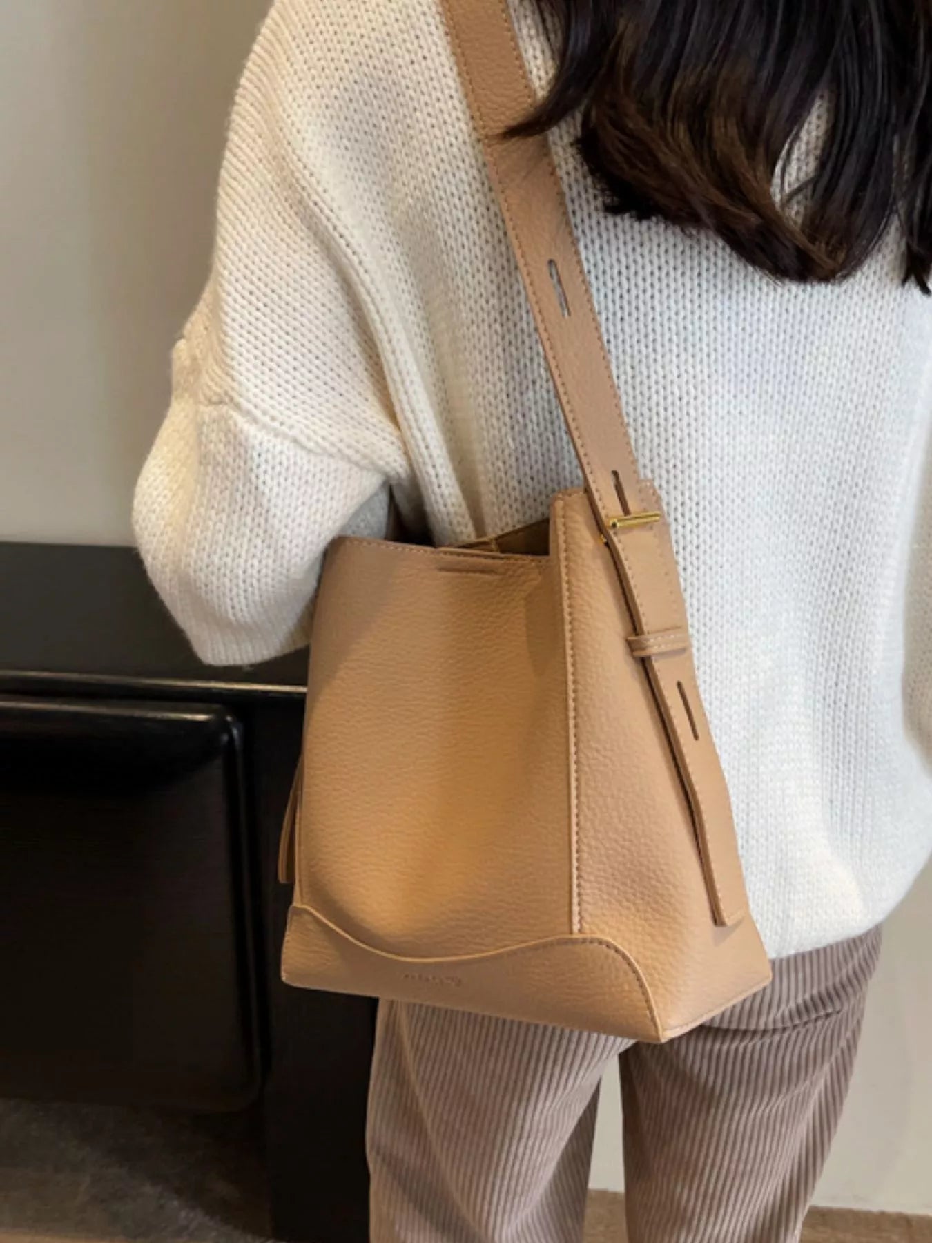 Khaki leather crossbody bag hanging at side with adjustable strap and zipper