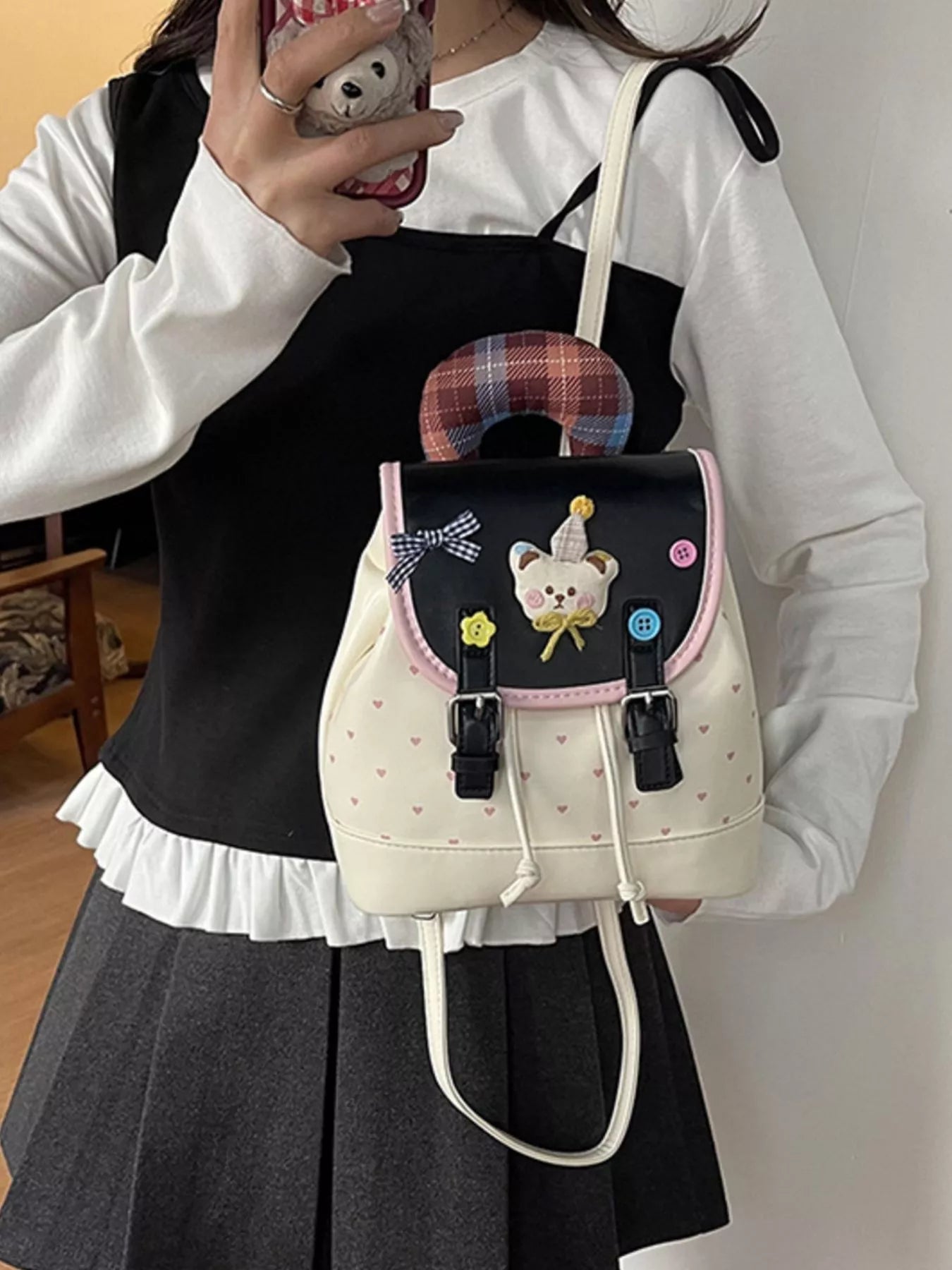 Beige cartoon bear backpack with plaid handle and front buckle straps, worn over dress