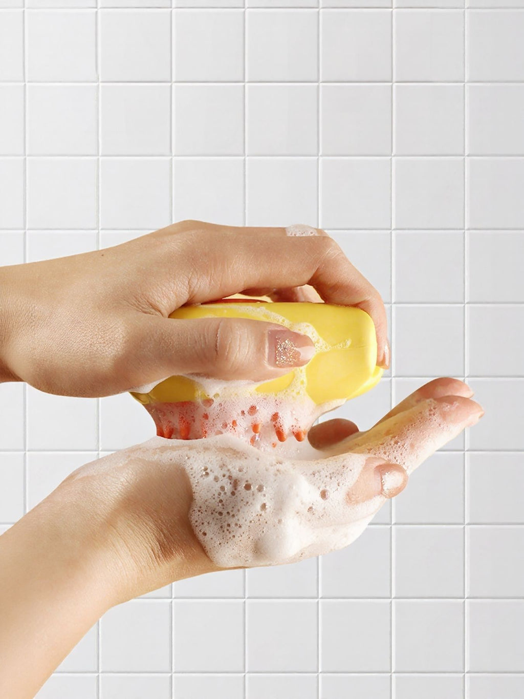 Hands lathering the yellow pet shower brush; suds on the orange bristle area