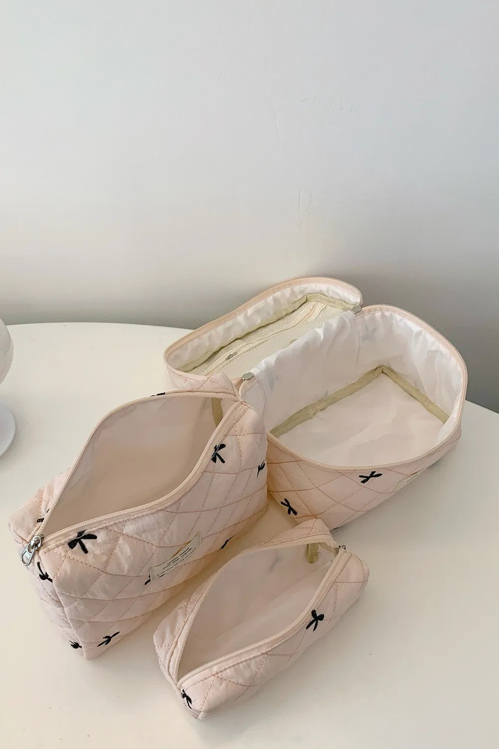 Beige quilted storage bag set with bow print; fabric handles and open zip tops.