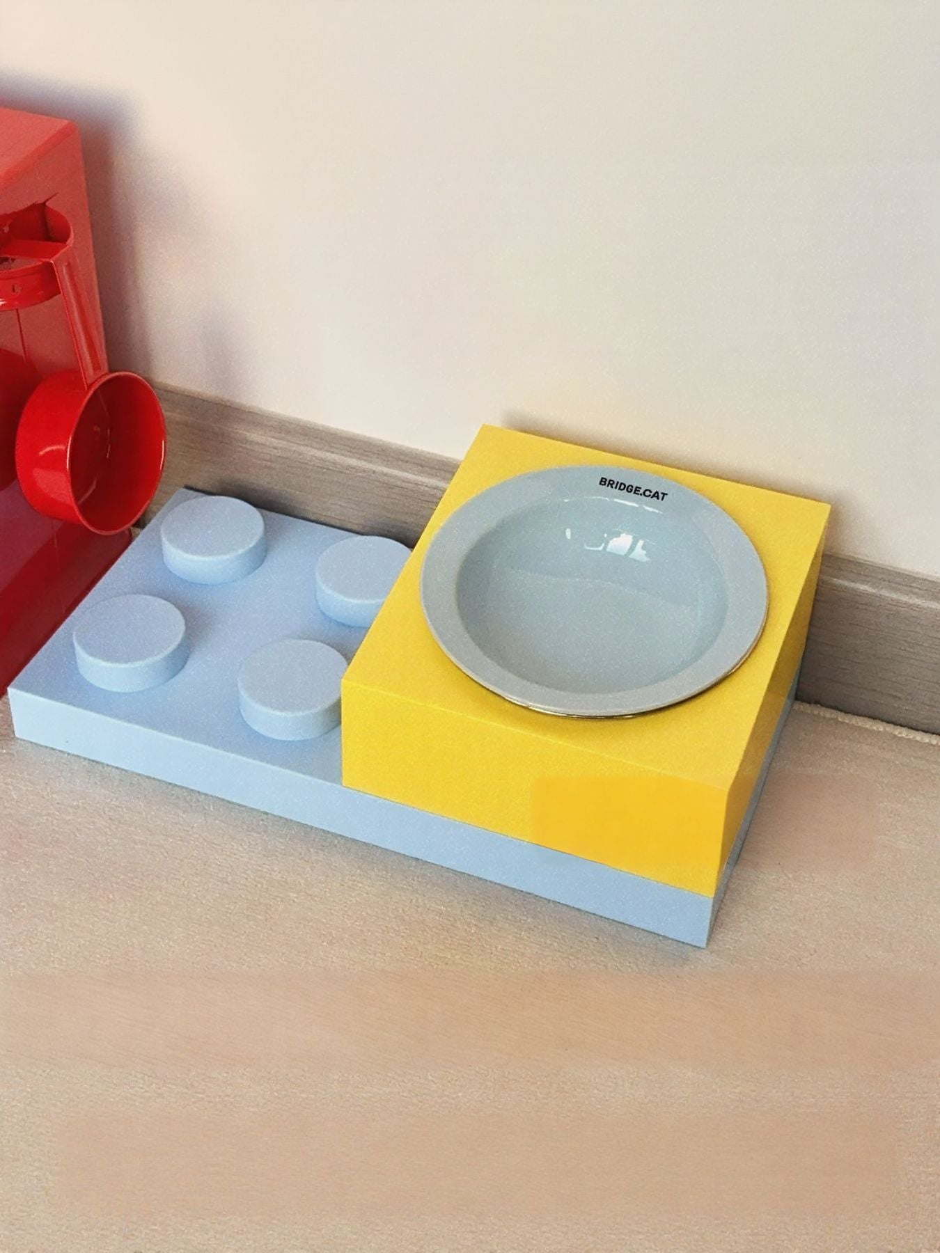Light blue pet food bowl with gray interior on yellow base near red container