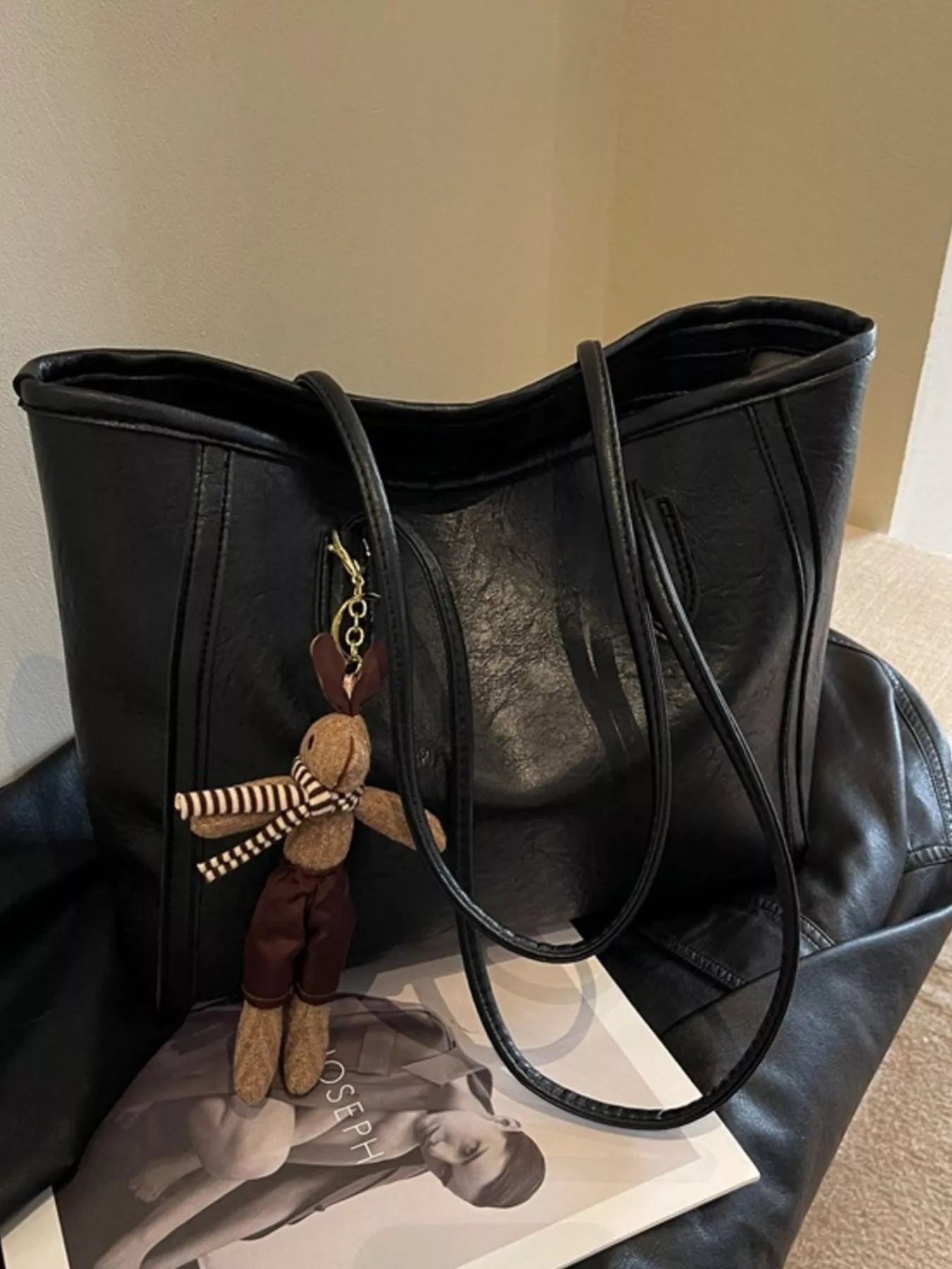 Black leather tote bag with top handles, visible side seam details, hanging plush keychain