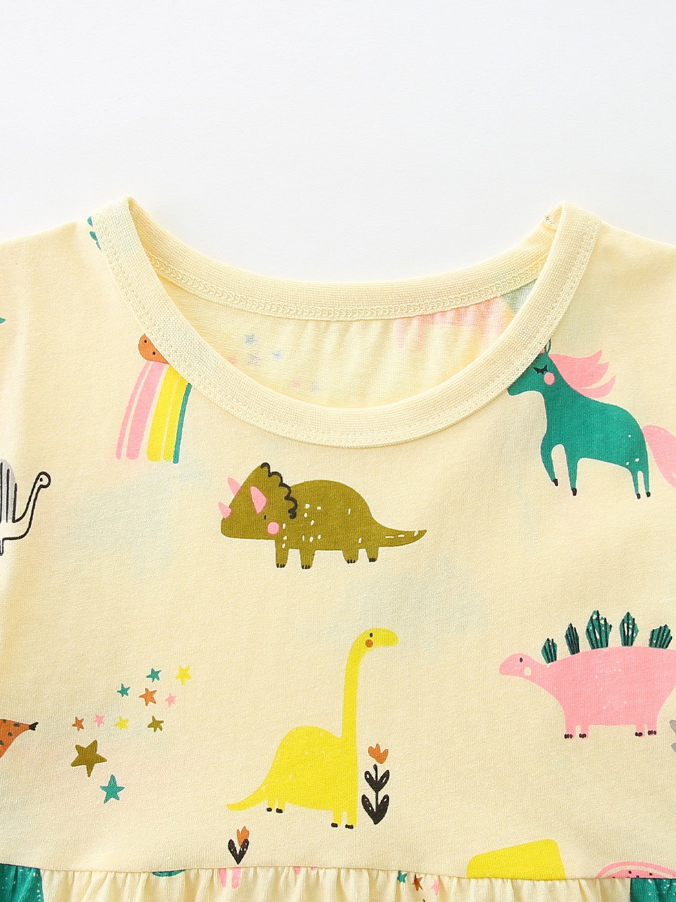 Pastel yellow crew-neck dress close-up with dinosaur and rainbow pattern