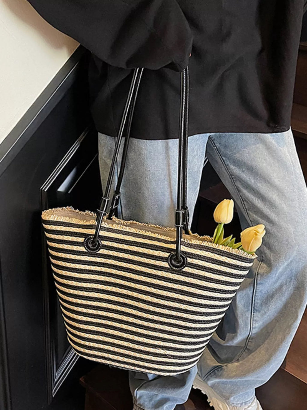 Black striped woven straw tote with long black handles and compact rounded shape
