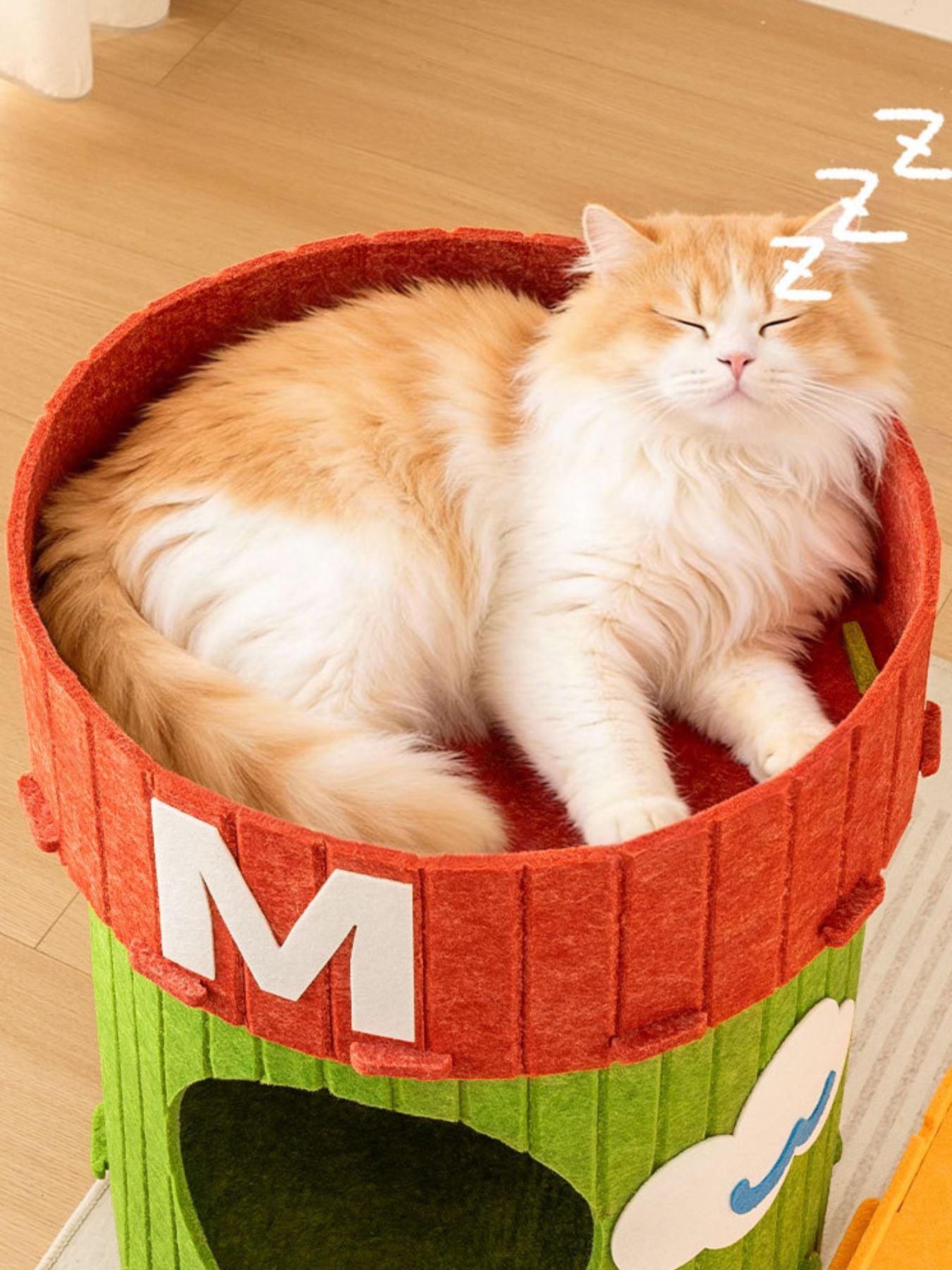 Red barrel cat house with a curled orange tabby sleeping inside, M front panel