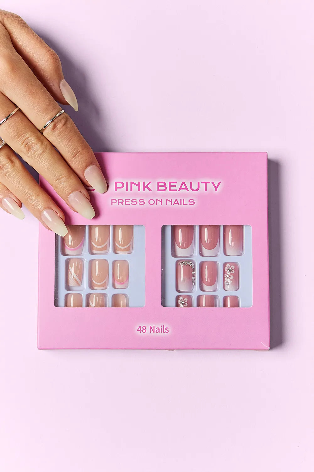 Hand wearing press-on nails next to SO PINK BEAUTY box, 48 nails assortment