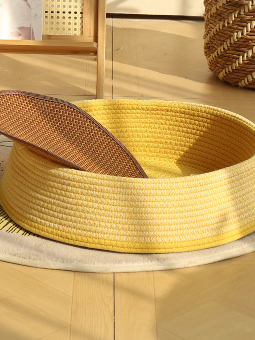 Woven rattan pet nest with yellow woven body and open top, beige cushion visible