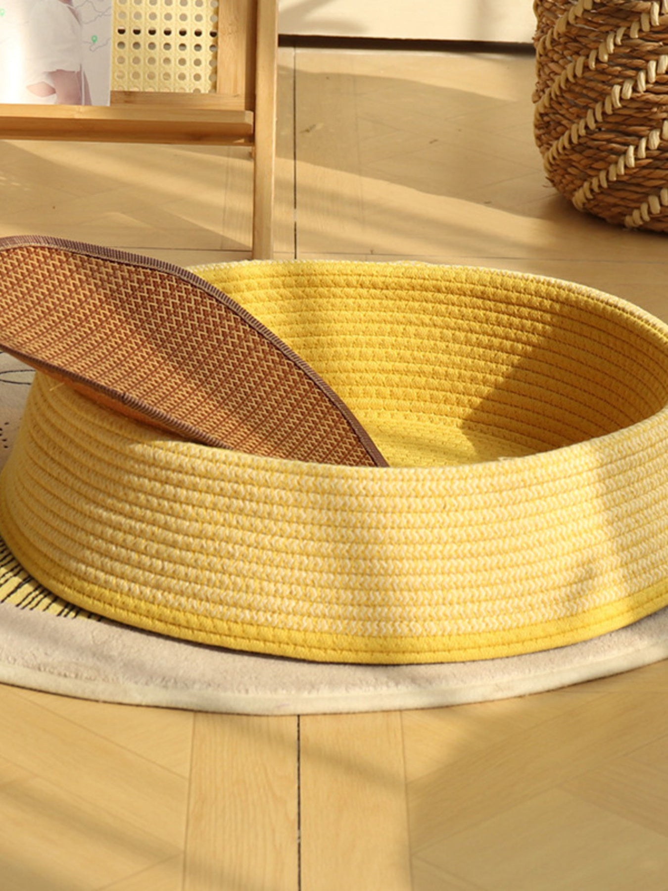Woven rattan pet nest with yellow woven body and open top, beige cushion visible