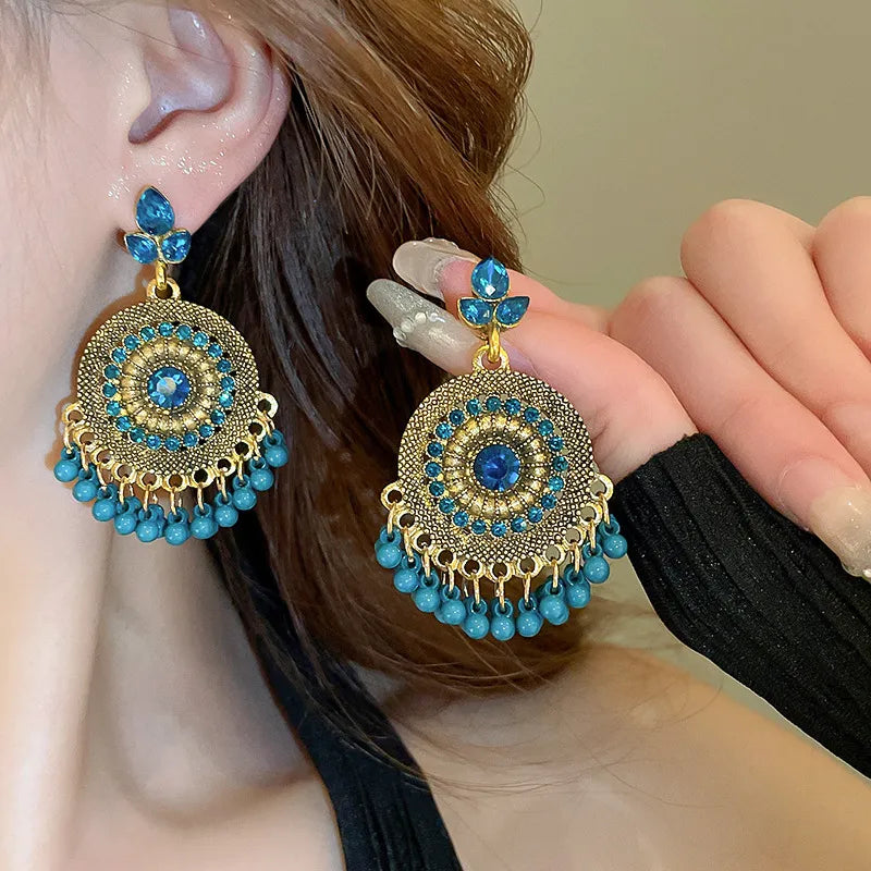 Cerulean blue rhinestone dangle earrings with round medallion, bead fringe, and bow tops