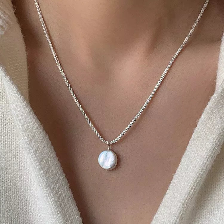 Silver chain necklace with round pearl pendant centered on neckline