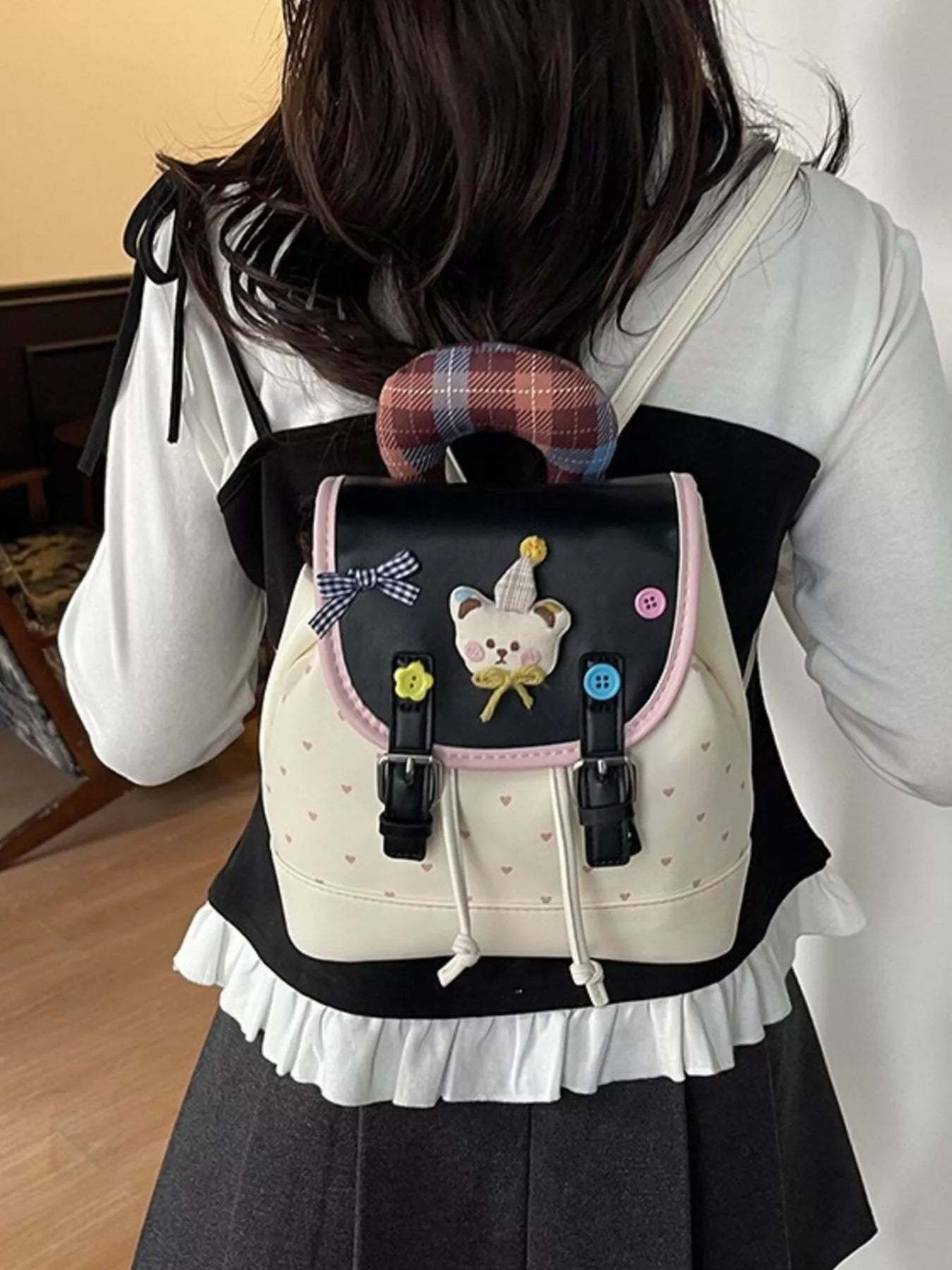 Beige backpack worn on back: front bear patch, plaid handle, dual side straps