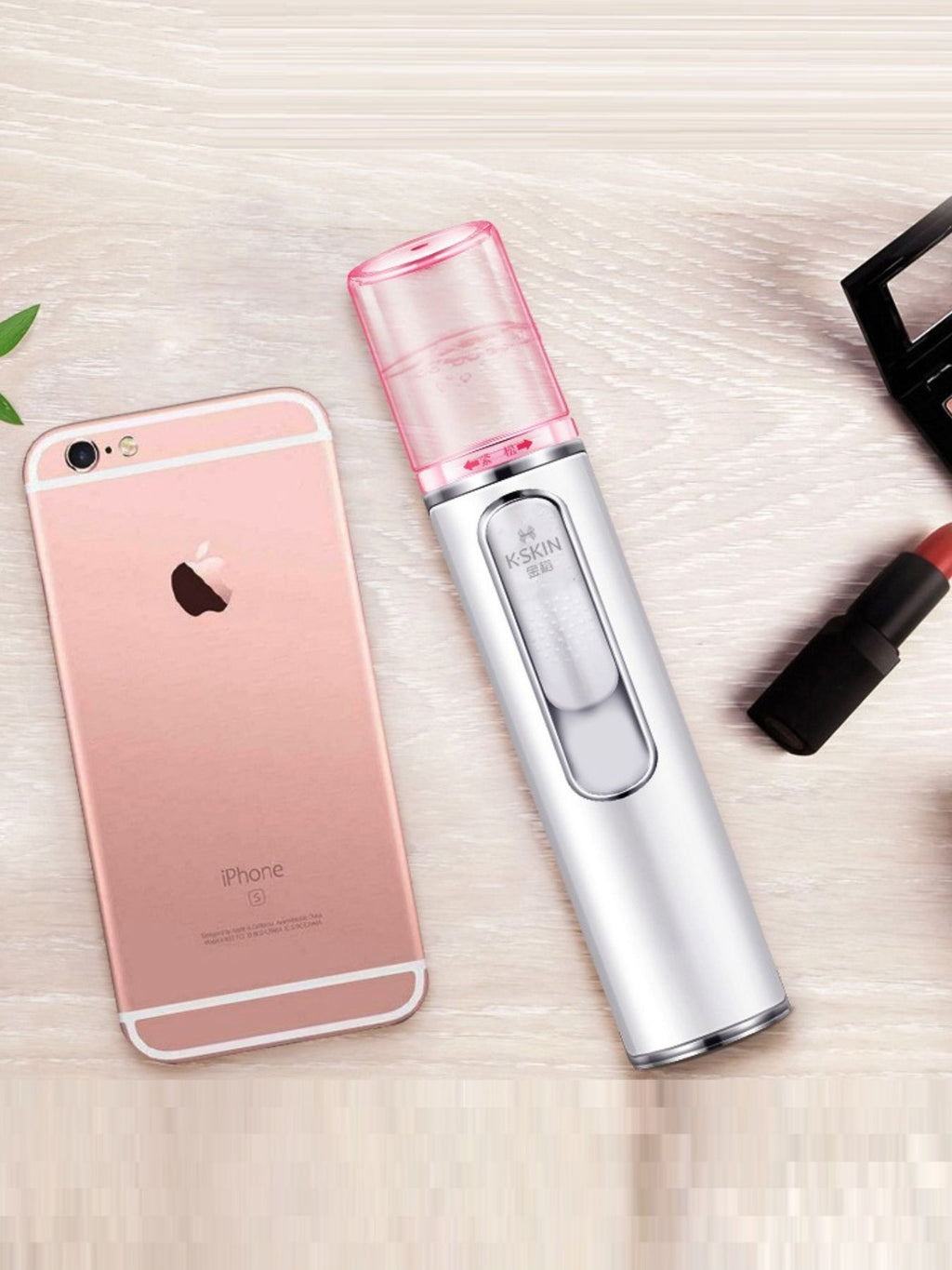Facial mister sprayer next to smartphone on tabletop; pink nozzle cap, white body