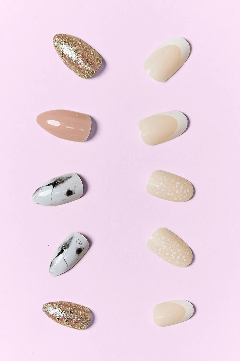 Assorted press-on nail tips: nude, gold glitter, white/black details, and beige