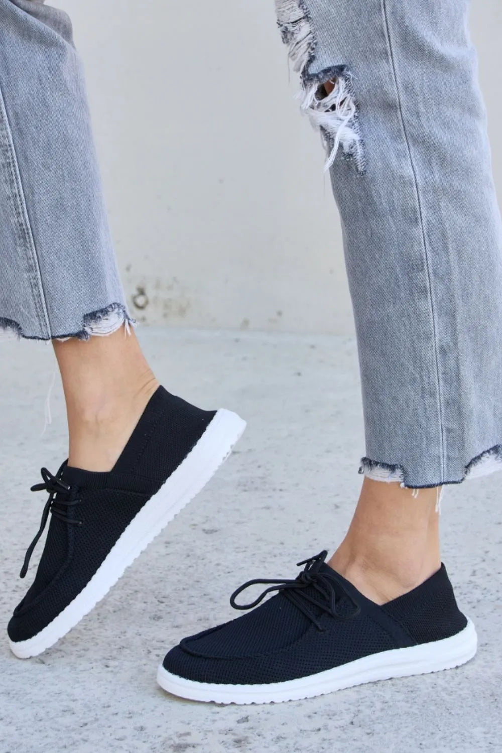 Black slip-on style sneakers with lace-up detail and white sole