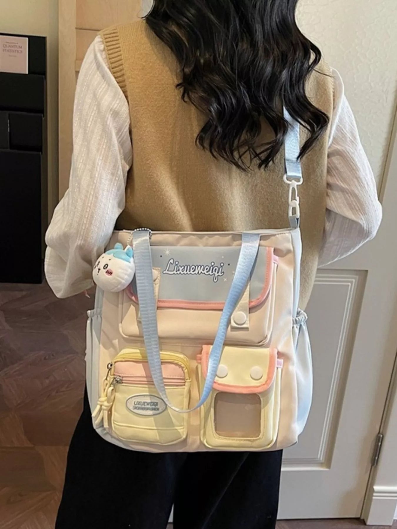 Multi-pocket shoulder bag worn on shoulder with pastel blue strap and plush front charm