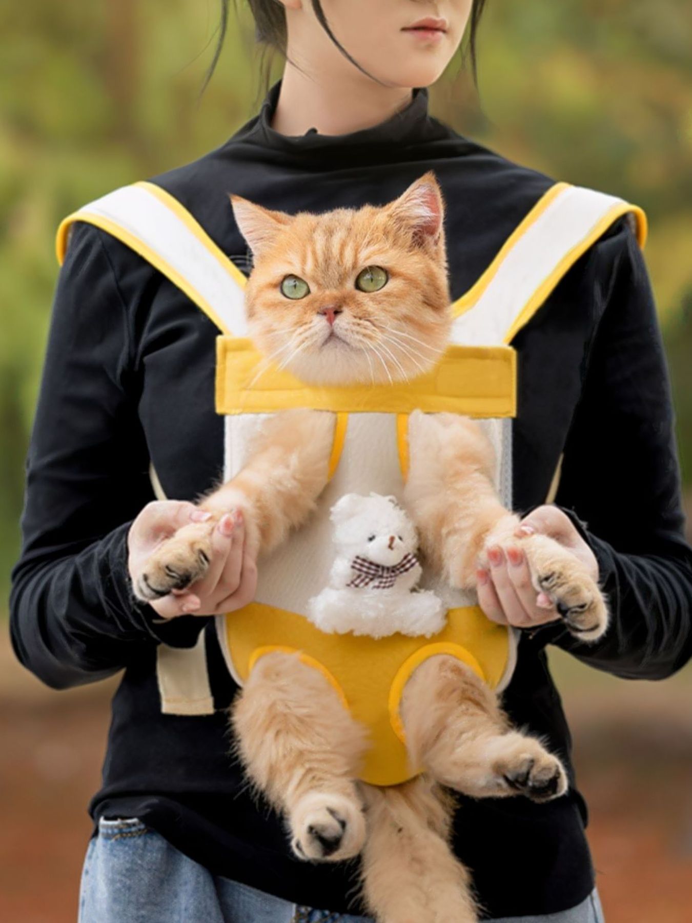 Yellow front pet carrier with mesh window, cat peeking out over a black jacket