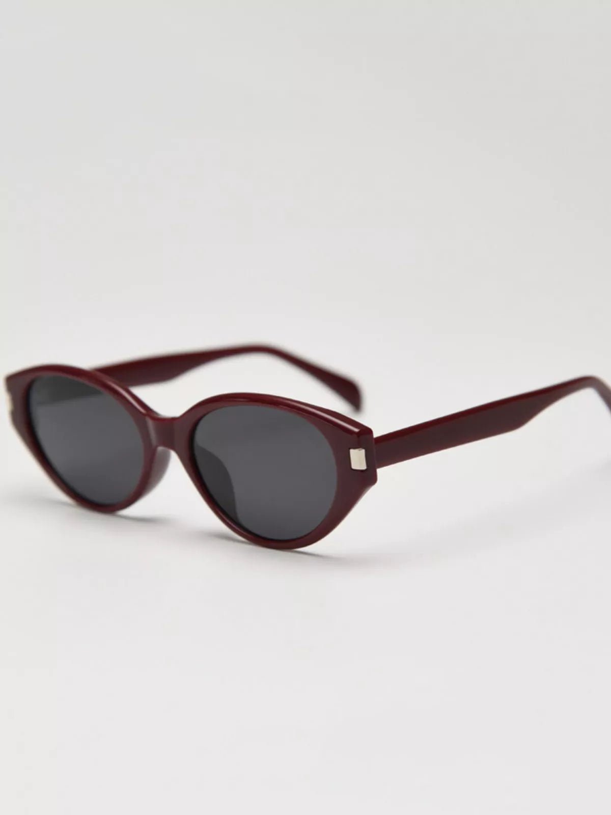 Dark red cat-eye sunglasses with black lenses, slim temples, and square metal detail