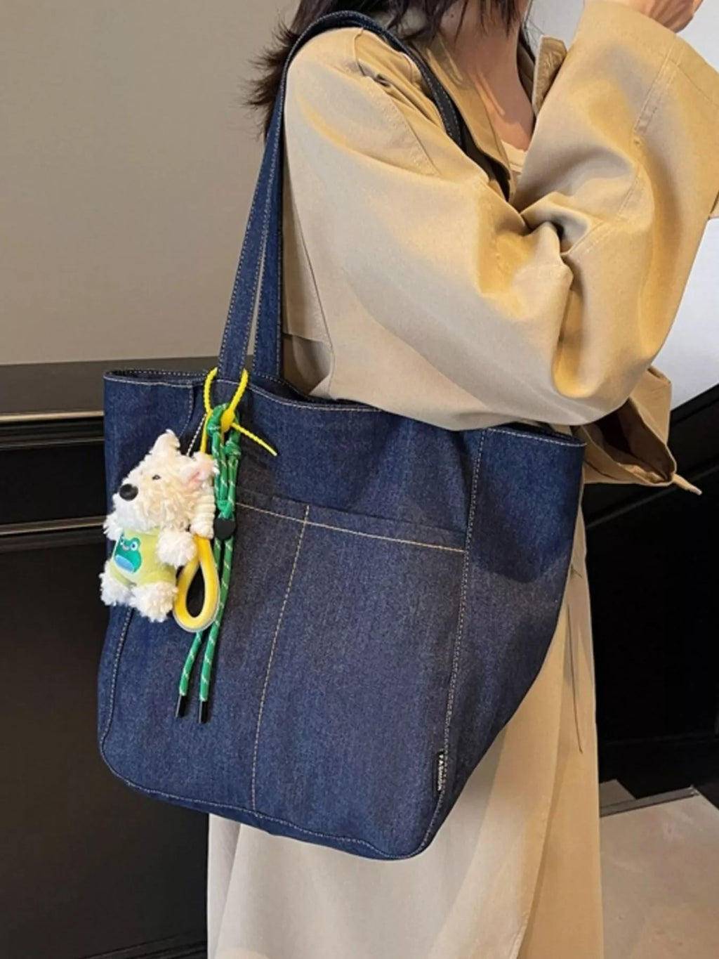 Dark navy denim tote held in hand, large front panel and hanging plush charm