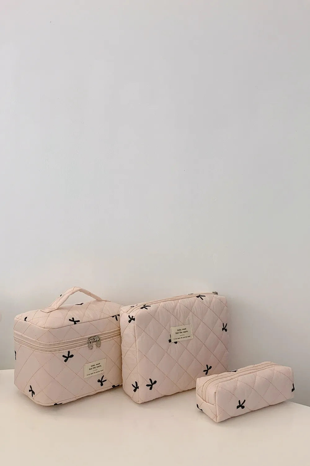 Beige quilted storage bag set with bow print, zip closures and label patches.