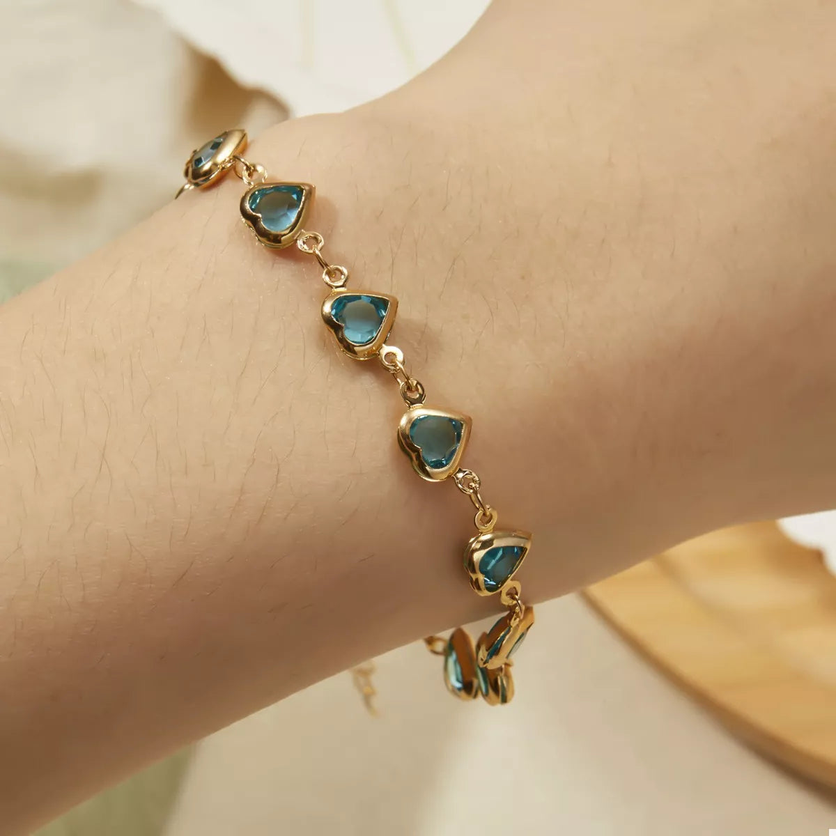 On-wrist view: gold-plated bracelet with teal heart charms on linked chain