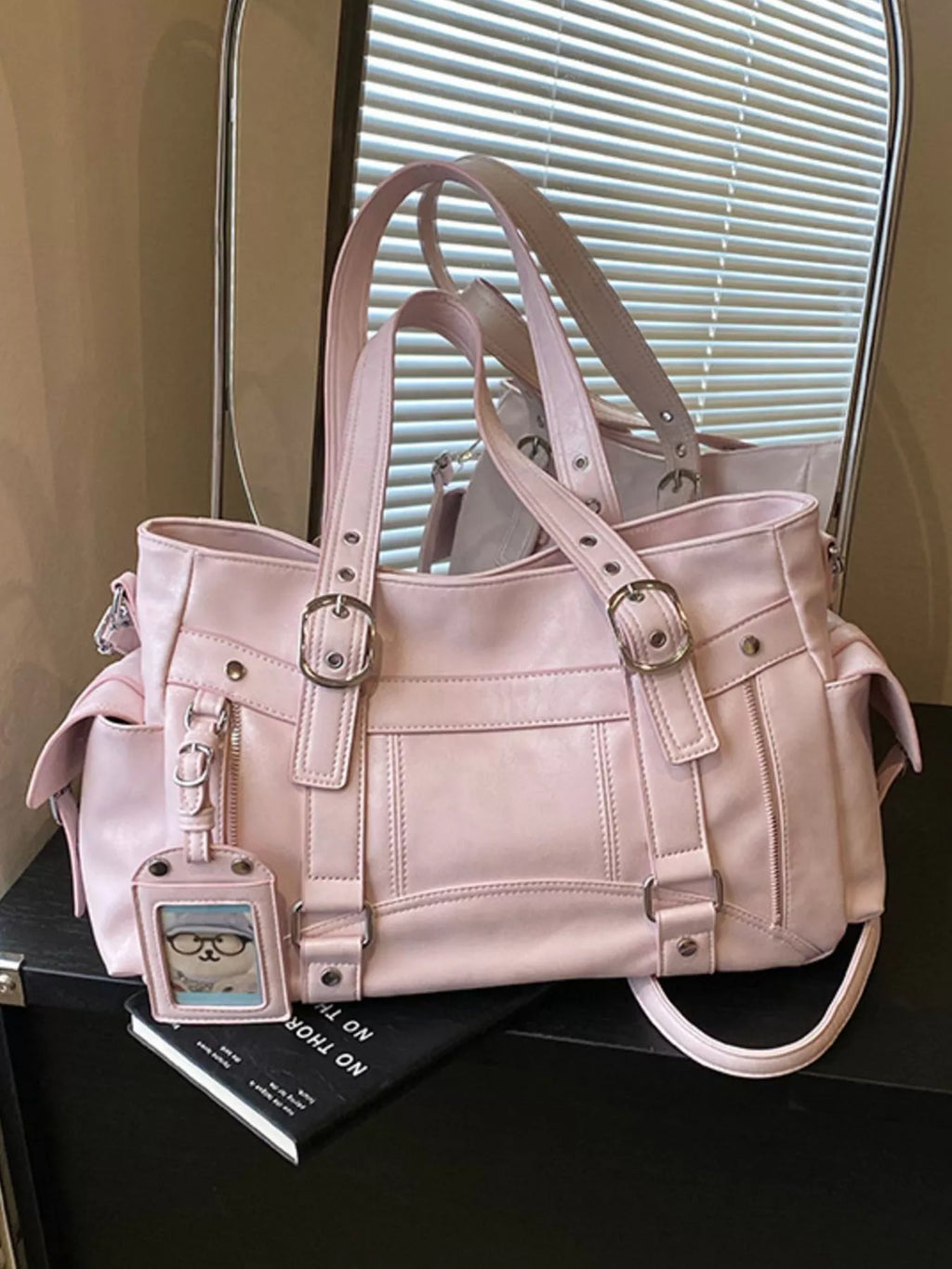 Pink shoulder bag with double straps, zipper compartments, and hanging charm tag