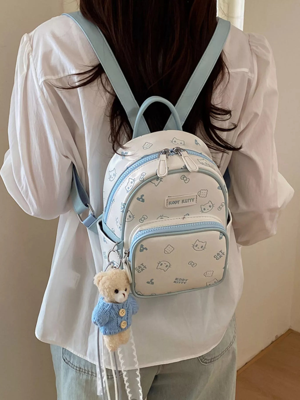 Pastel blue cat-pattern mini backpack worn with wide shoulder straps and front pocket