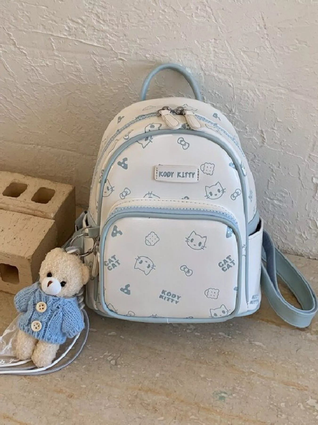 Pastel blue mini backpack with cat pattern, front zipper panel, and detachable wrist strap