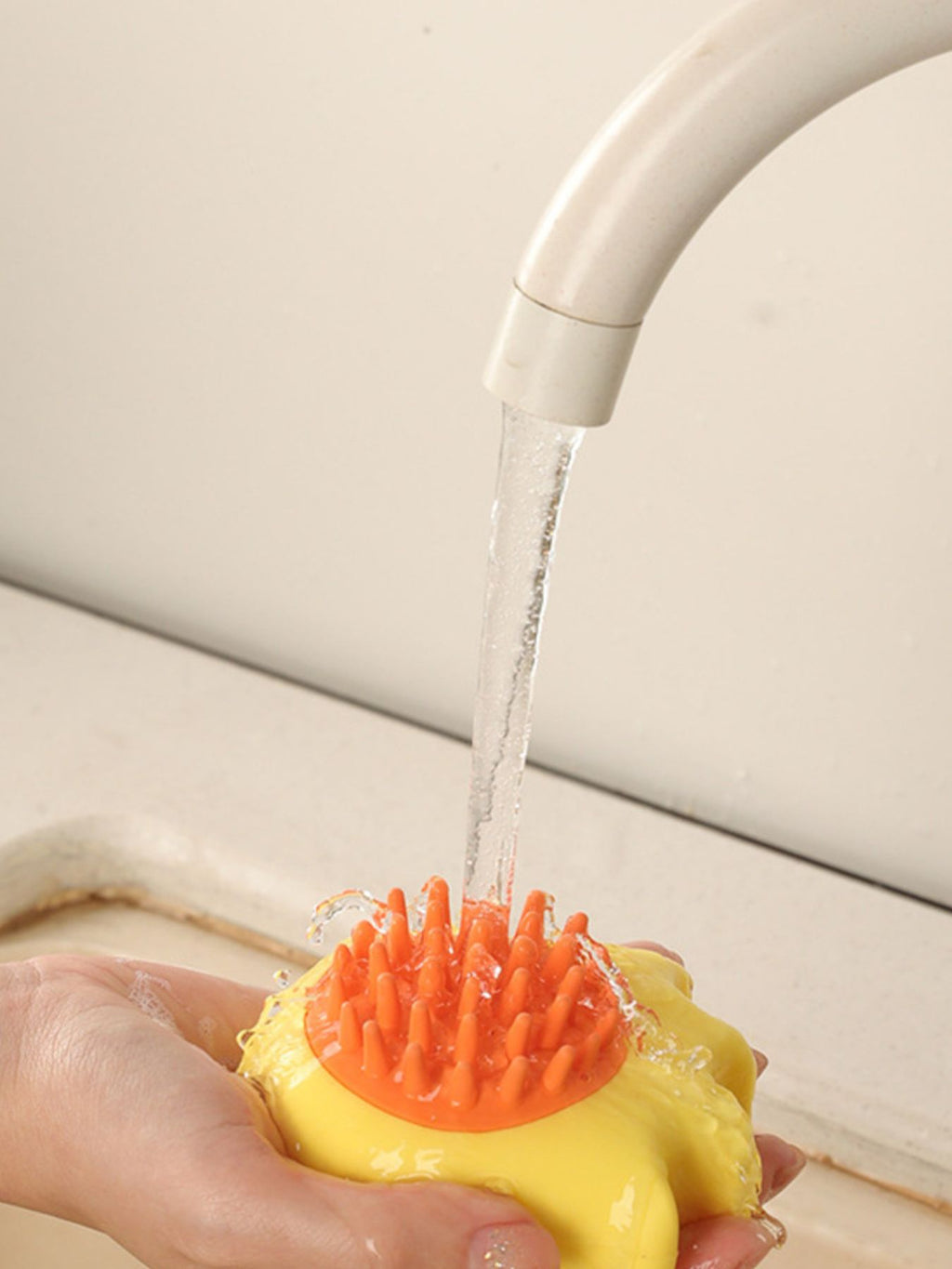 Yellow pet shower brush being rinsed under a stream of water, bristles visible