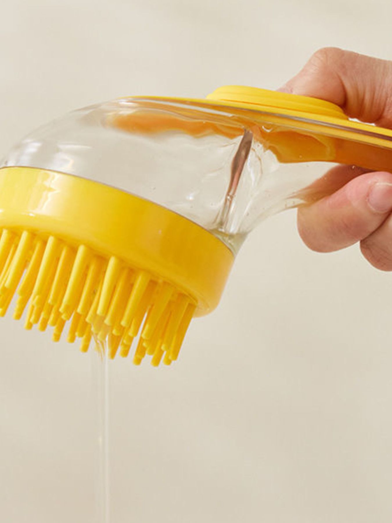 Yellow Soft Pet Shower Brush being held, clear body with bristle-covered round head