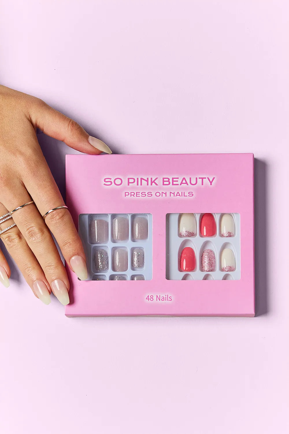 SO PINK BEAUTY press-on nails set in pink box; hand shows nude, glitter, and floral designs