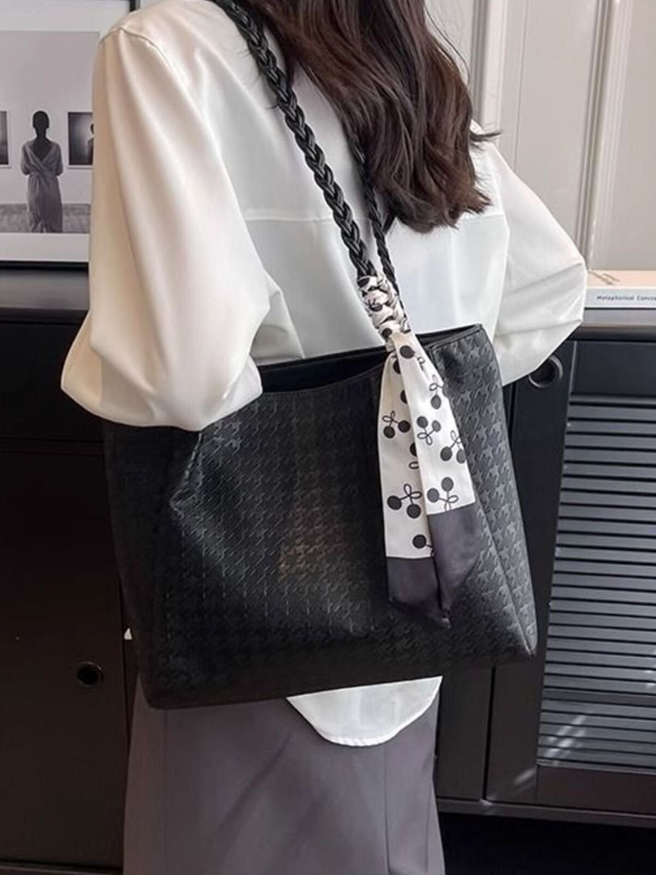 Black braided handle tote bag with ribbon tie, held over shoulder by model