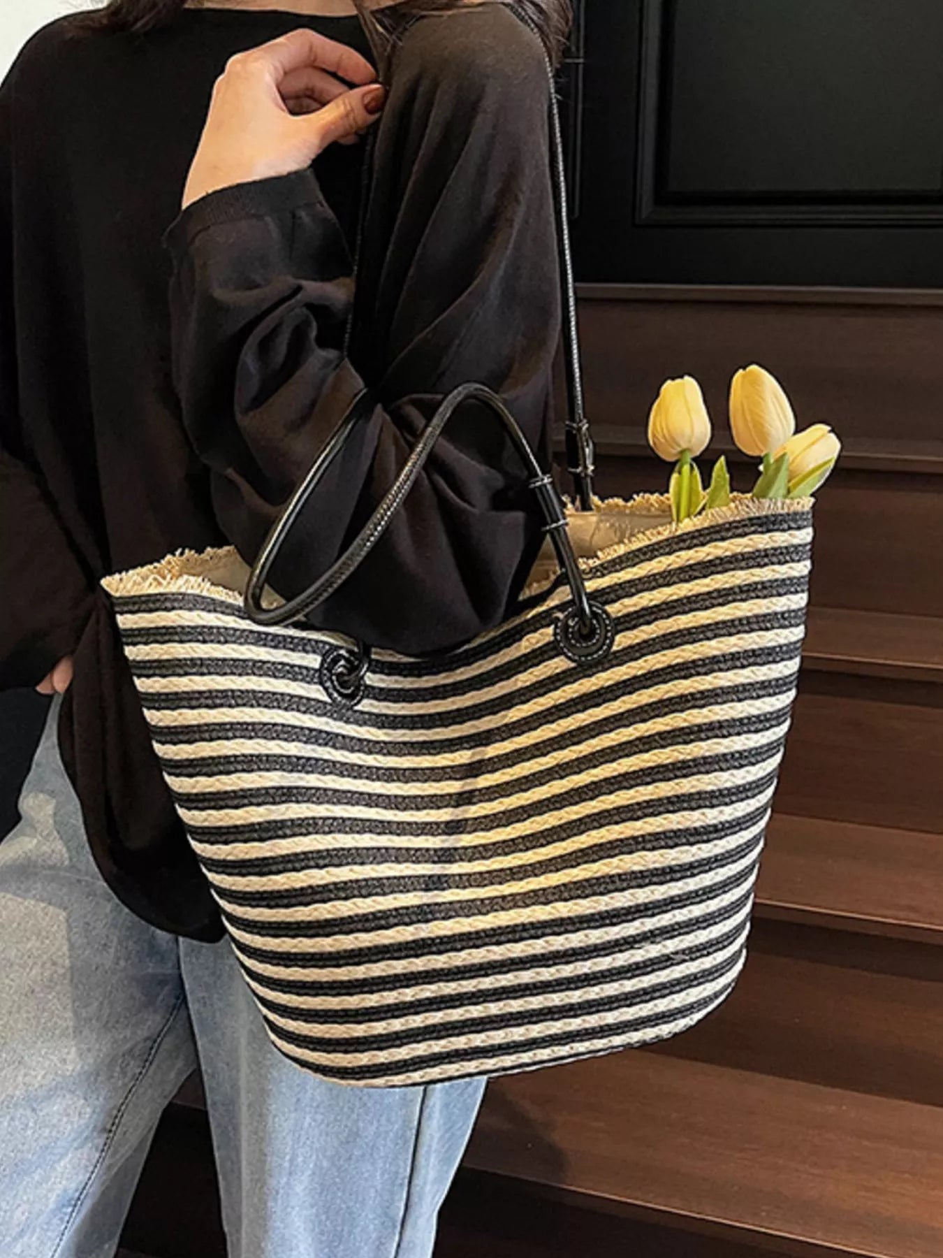Black-and-cream striped woven straw tote bag held by black shoulder straps