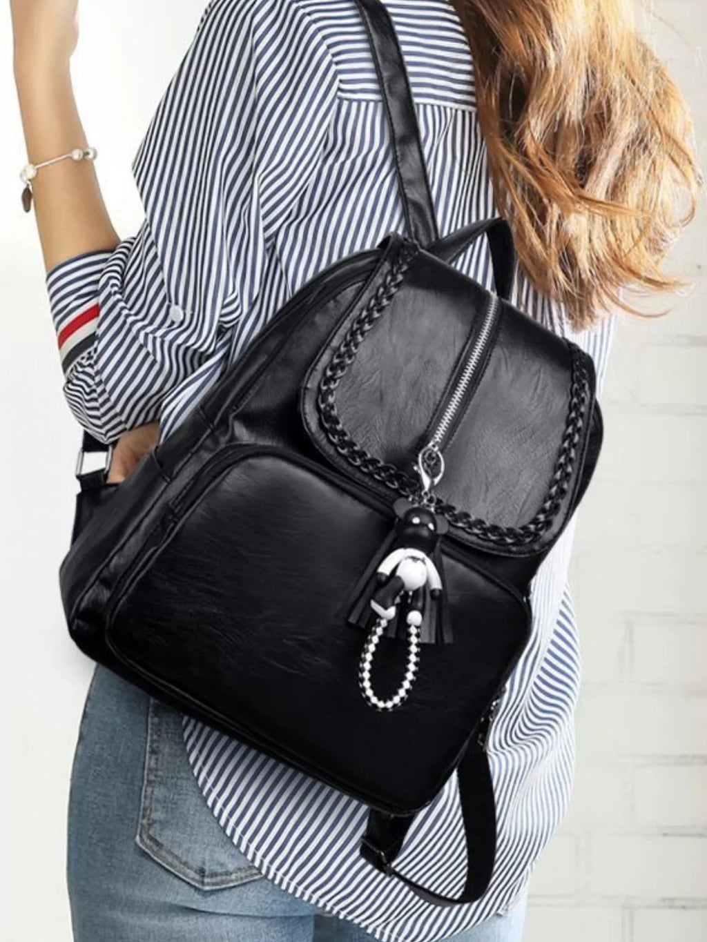Black leather backpack bag side view with braided trim flap and hanging bead keychain