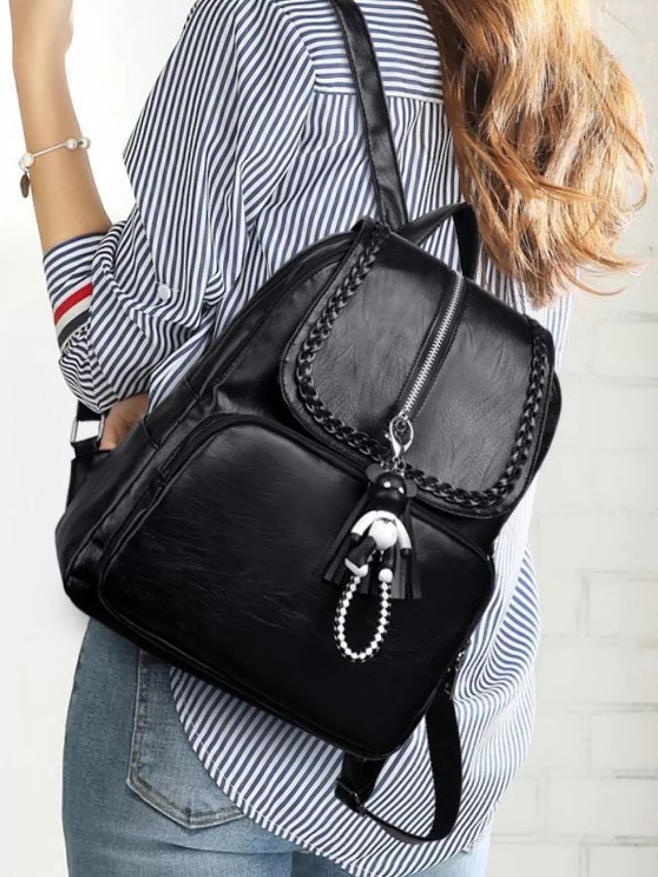Black leather backpack bag side view with braided trim flap and hanging bead keychain