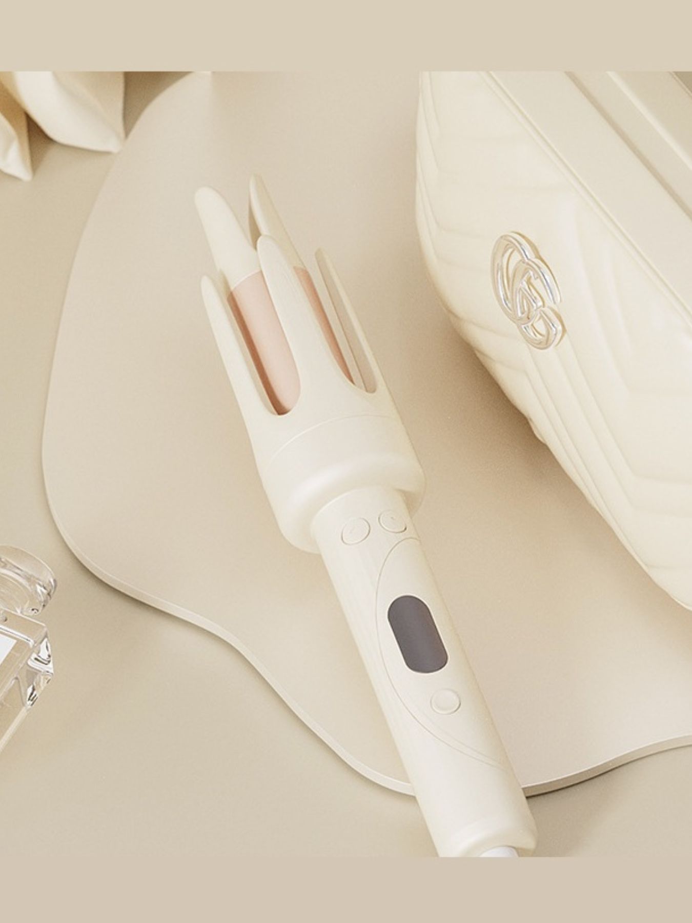 Beige automatic hair curling iron lying down, showing handle controls and three barrels
