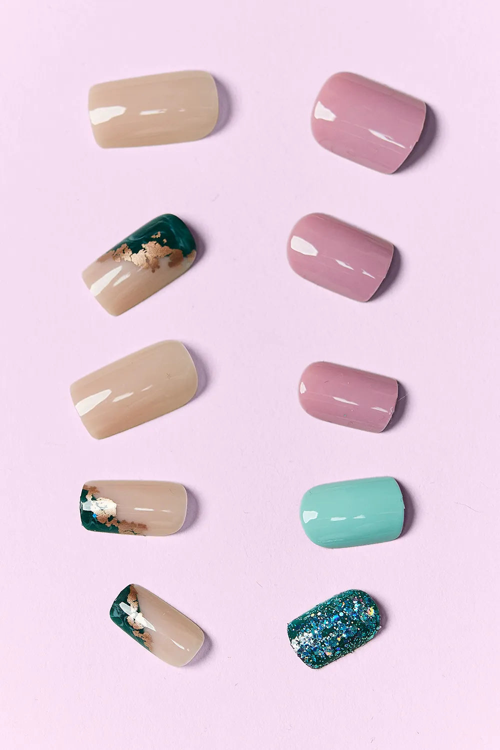 Assorted press-on nail tips: nude, pink, teal, green glitter, and bronze