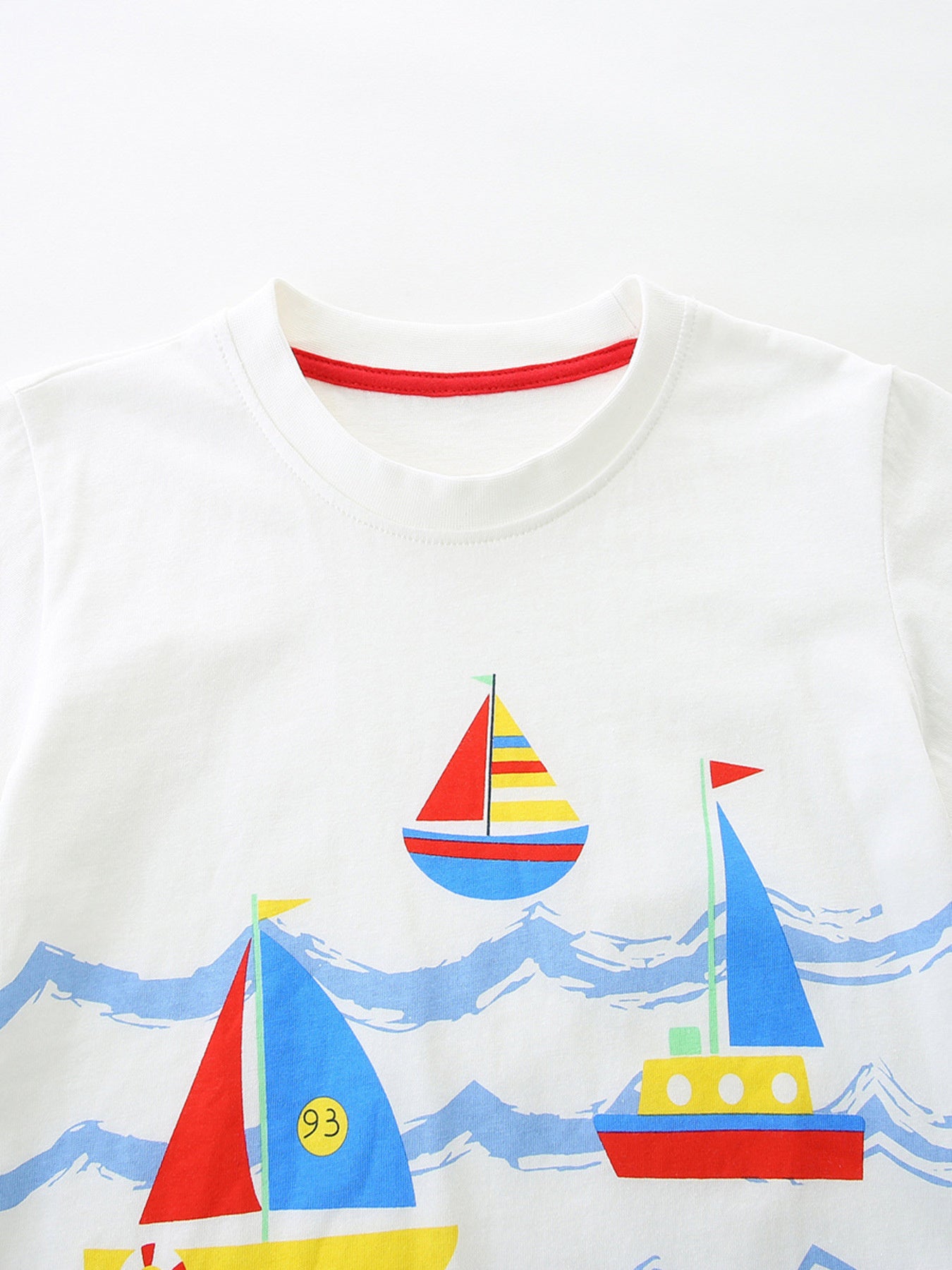 White tee close-up: sailboat and ocean waves print with small red neck trim