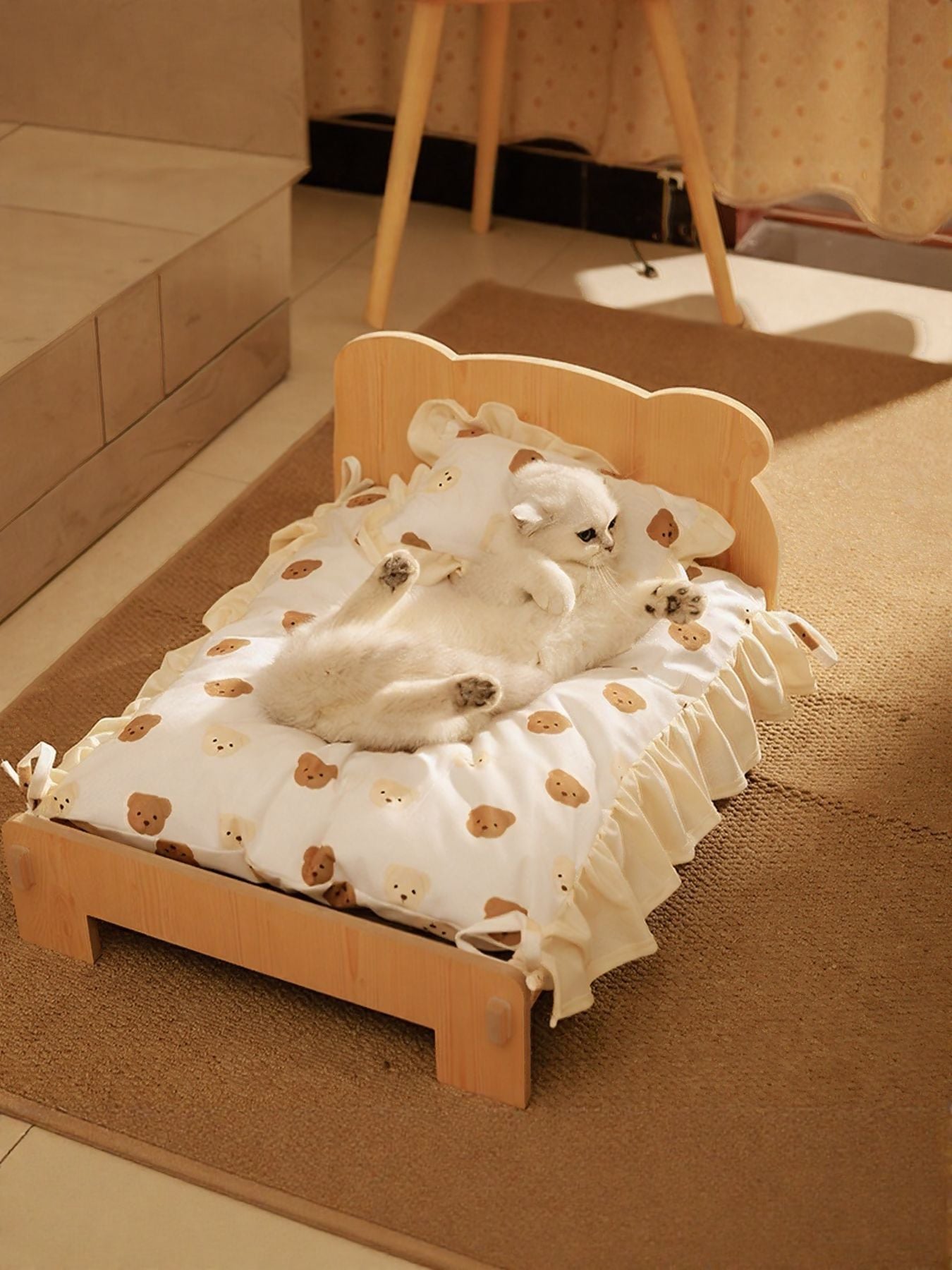 Wooden pet bed with bear-print blanket and ruffled trim, two cats lounging together.