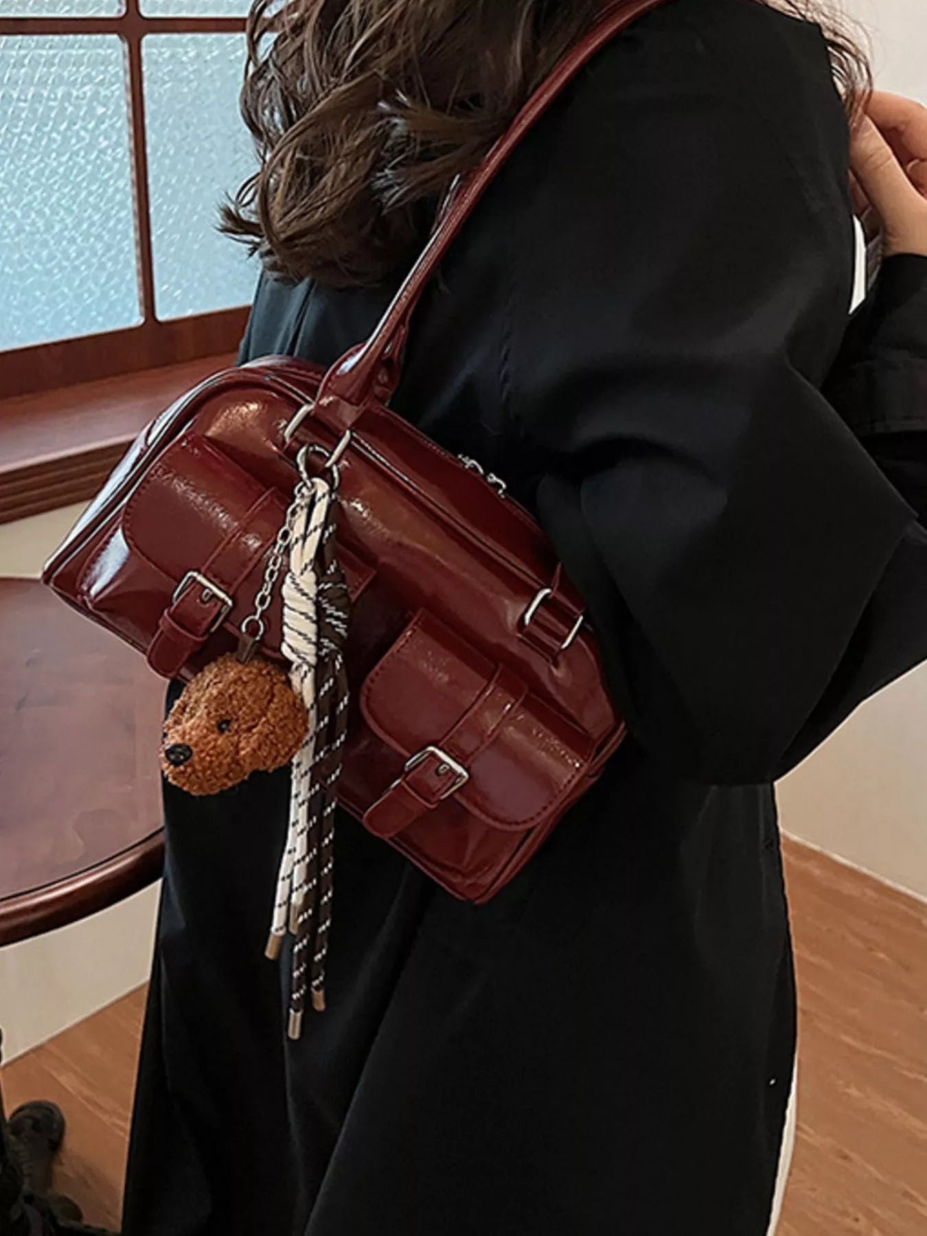 Deep red shoulder bag with adjustable strap, teddy keychain charm, and front buckled accents