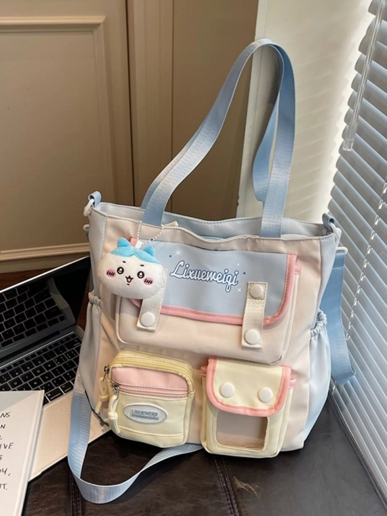 Multi-pocket shoulder bag showing plush keychain and top handle with pastel blue strap