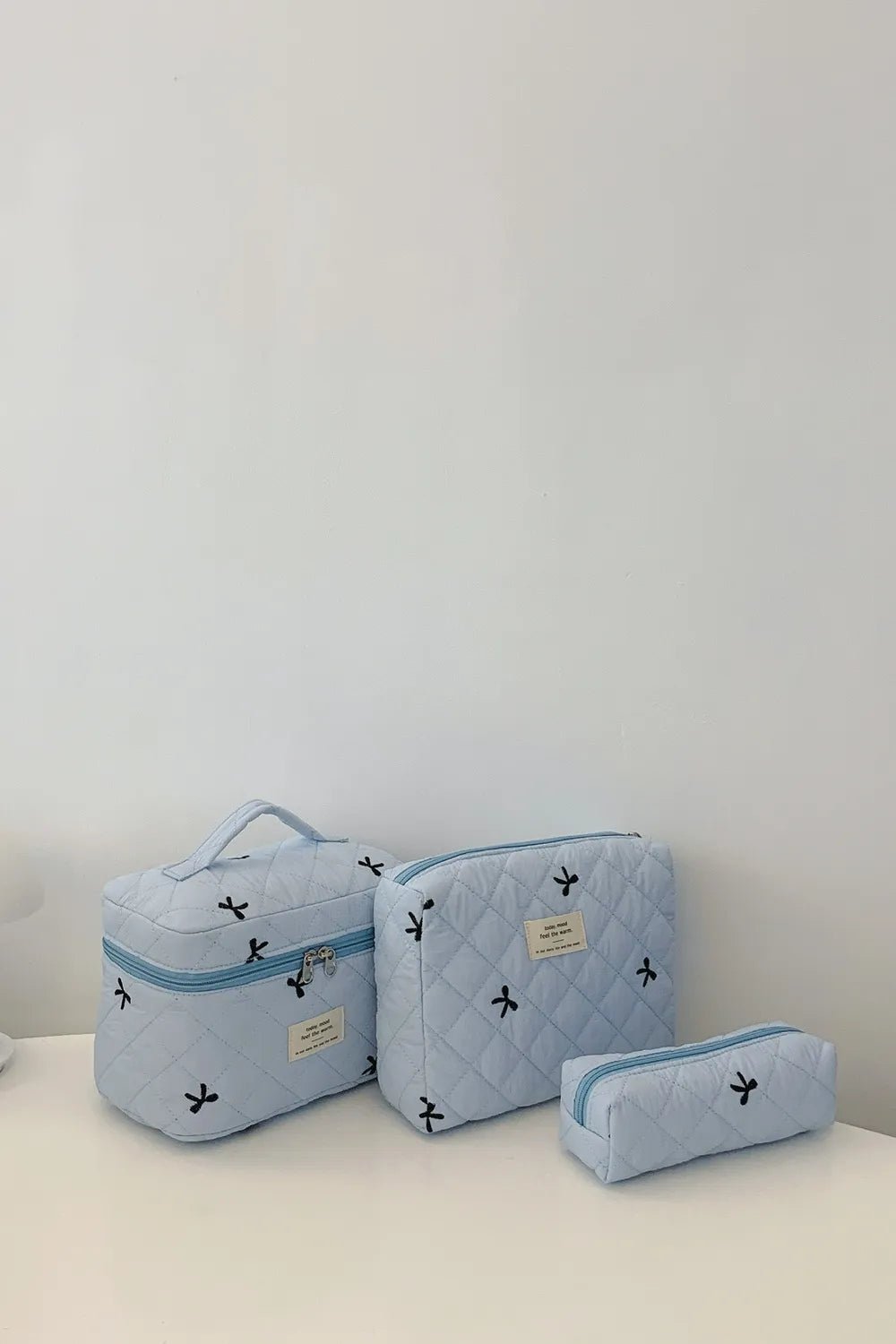 Light blue quilted storage bag set with bow pattern: large, medium, and small zip pouches