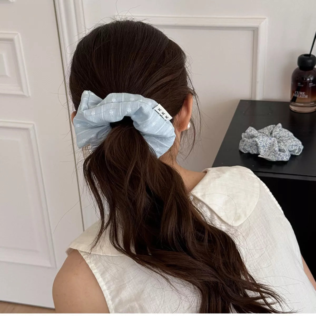 Light blue fabric hair scrunchie with small marks, on dark hair