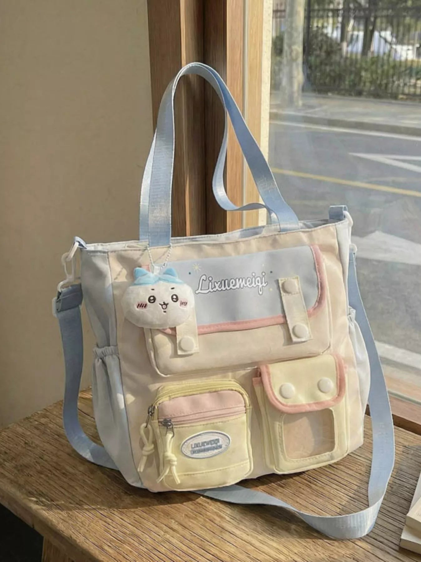 Multi-pocket shoulder bag in light neutral tones with pastel blue strap and front pockets